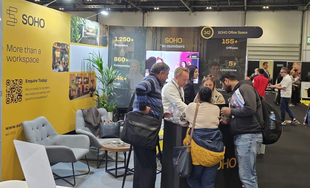 Business professionals networking at SOHO Office Space exhibition booth.