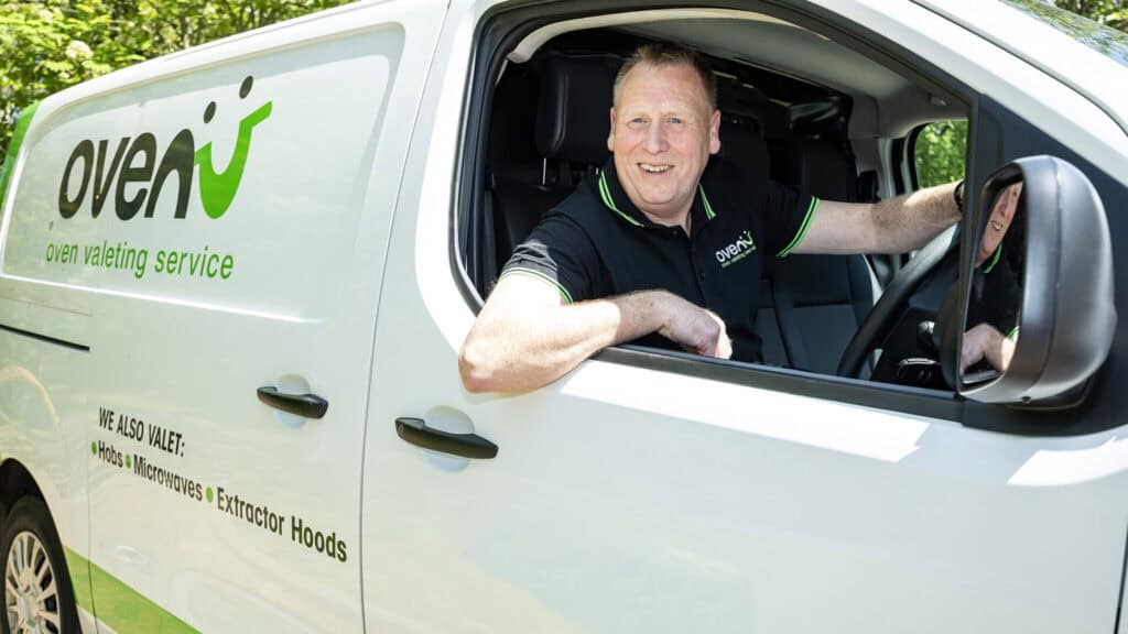 Oven valeting service vehicle with technician smiling inside.